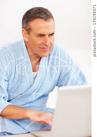 Bathrobe, relax and mature man on laptop, checking email, social media or streaming subscription on sofa. Internet website, couch and senior person on computer, morning and networking in living room. Bathrobe, relax and mature man on laptop, checking email, social media or streaming subscription on sofa. Internet website, couch and senior person on computer, morning and networking in living room. 139298971