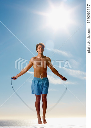Man, shirtless or rope skipping for fitness in summer workout, muscle or happy on vacation. Model, smile or training for natural glow of sport, cardio exercise or sunshine holiday by sky background Man, shirtless or rope skipping for fitness in summer workout, muscle or happy on vacation. Model, smile or training for natural glow of sport, cardio exercise or sunshine holiday by sky background 139299237
