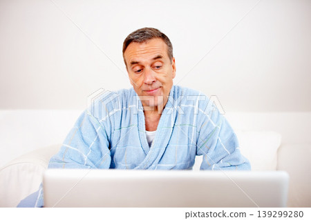 Gown, morning and mature man on laptop reading email, social media or streaming subscription on sofa. Internet search, couch and senior person in bathrobe on computer, website or networking in home. Gown, morning and mature man on laptop reading email, social media or streaming subscription on sofa. Internet search, couch and senior person in bathrobe on computer, website or networking in home. 139299280