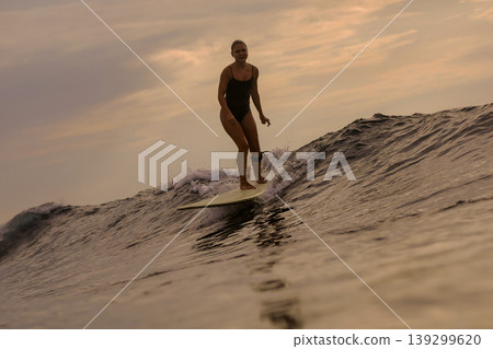 Woman Surfs Sunset, Sunset Illuminates Ocean As Woman Surfs Closer Woman Surfs Sunset, Sunset Illuminates Ocean As Woman Surfs Closer 139299620