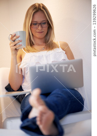 Woman, laptop and journalist with coffee in relax on chair reading, typing or writing in living room at home. Female person or freelancer smile on computer with cup of tea in remote work at house 139299626