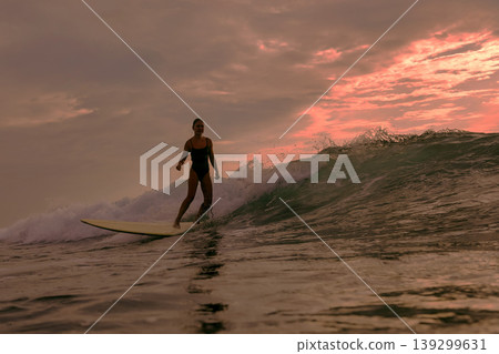 Graceful Female Surfer Enjoying Tranquil Sunset On Her Longboard Graceful Female Surfer Enjoying Tranquil Sunset On Her Longboard 139299631