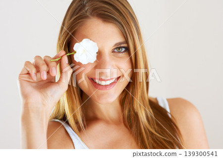 Portrait, woman and smile with flower in studio for natural beauty, organic makeup and fresh spring perfume on white background. Face, model and cover eye with floral plants for sustainable skincare Portrait, woman and smile with flower in studio for natural beauty, organic makeup and fresh spring perfume on white background. Face, model and cover eye with floral plants for sustainable skincare 139300541