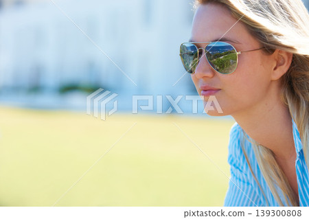 Woman, face and smile outdoor with sunglasses for relax, peace and beach in summer for vacation or holiday. Person, happy and eyewear or shades by ocean or sea for scenery, adventure or carefree 139300808
