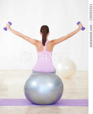 Woman, back and exercise on ball, dumbbells and balance in gym, training and strong muscle in arms. Girl, workout and fitness with pilates, weightlifting and hard work for health, wellness and body Woman, back and exercise on ball, dumbbells and balance in gym, training and strong muscle in arms. Girl, workout and fitness with pilates, weightlifting and hard work for health, wellness and body 139301021