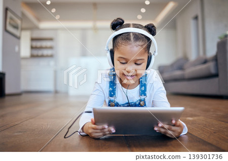 Kid, headphone and tablet for streaming in home with internet for entertainment, learning or watching. Little girl, lying and floor in living room for comfort with technology for online, web or app 139301736