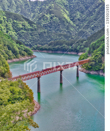 A hidden gem in Shizuoka: A red iron bridge and train floating on an emerald green lake. A hidden gem in Shizuoka: A red iron bridge and train floating on an emerald green lake. 139301935