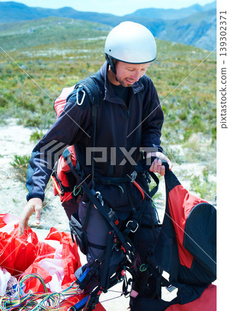 Sports, parachute and man in nature with equipment, safety preparation and helmet in paragliding exercise. Athlete, training or gear for outdoor adventure, backpack or happy wellness in countryside Sports, parachute and man in nature with equipment, safety preparation and helmet in paragliding exercise. Athlete, training or gear for outdoor adventure, backpack or happy wellness in countryside 139302371