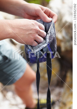 Person, rock climbing and hand in chalk bag for grip strength on mountain, danger challenge for rope adventure. Athlete, fingers and gear for sport training on cliff for safety, support or workout Person, rock climbing and hand in chalk bag for grip strength on mountain, danger challenge for rope adventure. Athlete, fingers and gear for sport training on cliff for safety, support or workout 139302392
