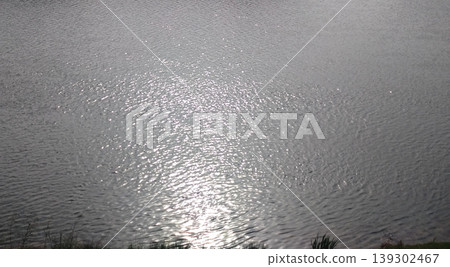 A textured background featuring the shimmering reflection of sunlight on the water's surface and gentle ripples. 139302467