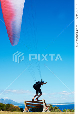 Man, parachute or paragliding sport in launch exercise, healthy adventure or extreme fitness for wellness. Person, preparation and fearless by bench for flight with helmet and safety gear by blue sky Man, parachute or paragliding sport in launch exercise, healthy adventure or extreme fitness for wellness. Person, preparation and fearless by bench for flight with helmet and safety gear by blue sky 139302492