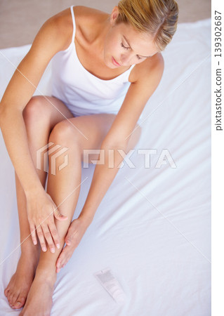 Woman, lotion and skincare for legs or hair removal in bedroom with treatment, hydration or soothing with top view. Person, dermatology and bodycare by waxing, shaving or epilation with cream 139302687