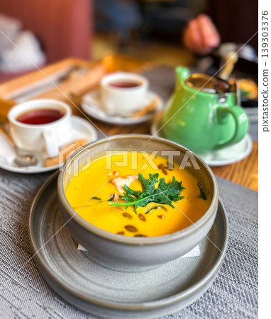 Pumpkin soup served on table. Pumpkin cream soup with seeds and greens. Cozy atmosphere. 139303376