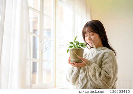 一位女士在窗邊欣賞植物。 139303410