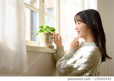 一位女士在窗邊看著室內植物。 139303443