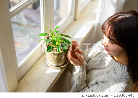 A woman touching a houseplant by the window. 139303445
