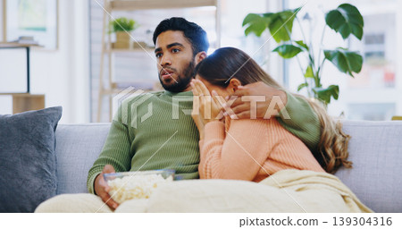 Fear, hug and couple watching tv on a sofa with popcorn for movie, film or streaming show at home. Wow, television and people embrace in living room with cinema snack for omg, horror or spooky series Fear, hug and couple watching tv on a sofa with popcorn for movie, film or streaming show at home. Wow, television and people embrace in living room with cinema snack for omg, horror or spooky series 139304316
