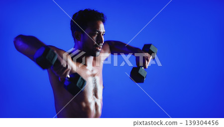 Fitness, weight training or man in studio with dumbbell, power or bicep lift in bodybuilding. Exercise, space or person on blue background with equipment, intense workout or strength in muscle gain. 139304456