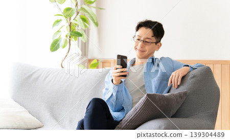 一名男子正舒適地躺在沙發上,一邊使用智慧型手機。 一名男子正舒適地躺在沙發上,一邊使用智慧型手機。 139304489