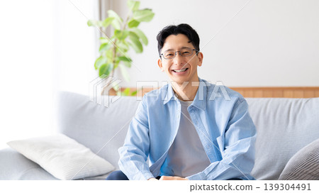 A smiling man sitting on the living room sofa. A smiling man sitting on the living room sofa. 139304491