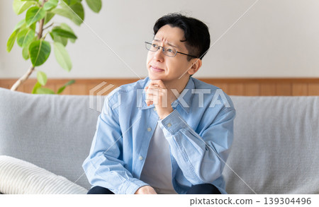 A man sitting on the living room sofa, thinking. A man sitting on the living room sofa, thinking. 139304496