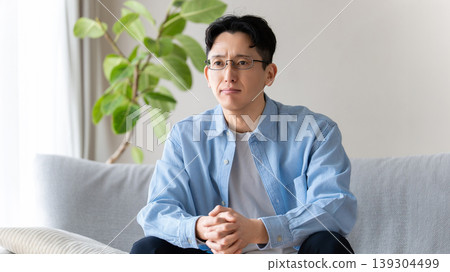 A man sitting on the living room sofa, thinking. A man sitting on the living room sofa, thinking. 139304499