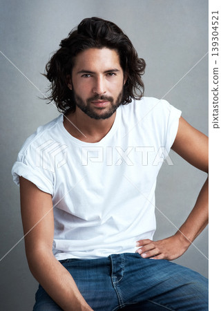 Style, serious and portrait of man in studio on a stool with casual, cool and stylish outfit. Confidence, handsome and young male model from Mexico with trendy clothes on chair by gray background. Style, serious and portrait of man in studio on a stool with casual, cool and stylish outfit. Confidence, handsome and young male model from Mexico with trendy clothes on chair by gray background. 139304521