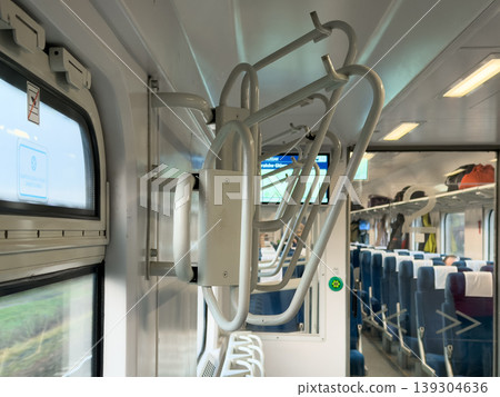 Interior view of a modern train car featuring luggage racks, comfortable seating, and grab handles for passenger convenience and travel Interior view of a modern train car featuring luggage racks, comfortable seating, and grab handles for passenger convenience and travel 139304636