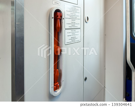 Orange emergency hand brake mechanism secured in white recessed housing on a train interior wall with multilingual instructions 139304641