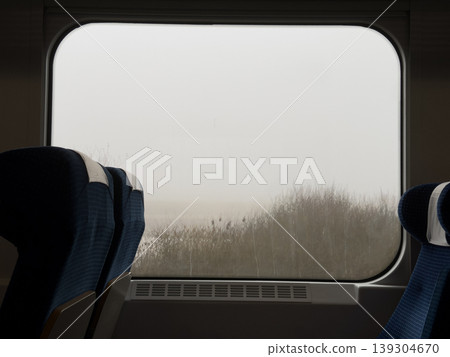 Empty blue fabric train seats face a hazy, muted landscape through a large window, evoking contemplation and journey Empty blue fabric train seats face a hazy, muted landscape through a large window, evoking contemplation and journey 139304670