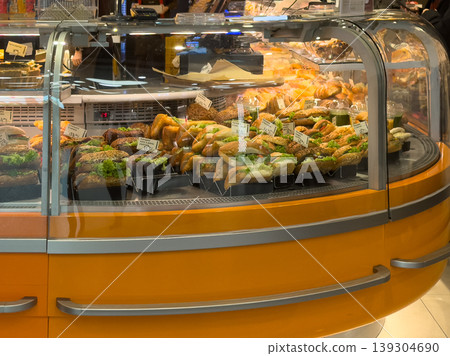 Freshly prepared sandwiches and baked goods displayed in a refrigerated bakery case, ready for sale to customers 139304690
