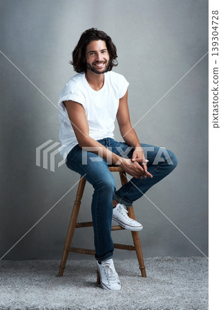 Fashion, smile and portrait of man in studio on a stool with casual, cool and stylish outfit. Happy, handsome and confident young male model from Mexico with trendy style on chair by gray background. 139304728