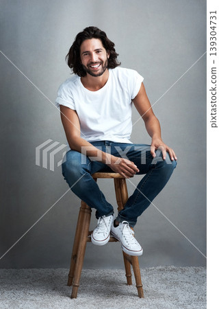 Fashion, happy and portrait of man in studio on a stool with casual, cool and stylish outfit. Smile, handsome and confident young male model from Mexico with trendy style on chair by gray background. Fashion, happy and portrait of man in studio on a stool with casual, cool and stylish outfit. Smile, handsome and confident young male model from Mexico with trendy style on chair by gray background. 139304731