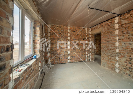 Interior of unfinished brick house with concrete floor and bare walls ready for plastering under construction. Real estate development Interior of unfinished brick house with concrete floor and bare walls ready for plastering under construction. Real estate development 139304840