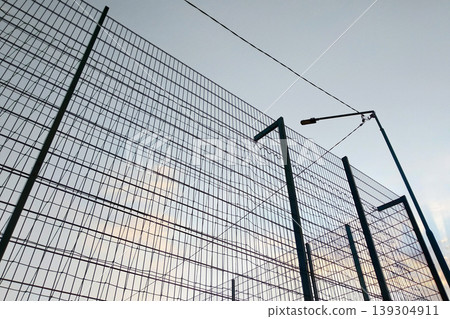 High wire mesh fence in restricted area on blue sky background. High wire mesh fence in restricted area on blue sky background. 139304911