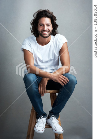 Fashion, smile and portrait of man in studio on a stool with casual, cool and stylish outfit. Happy, handsome and confident young male model from Mexico with trendy style on chair by gray background. Fashion, smile and portrait of man in studio on a stool with casual, cool and stylish outfit. Happy, handsome and confident young male model from Mexico with trendy style on chair by gray background. 139305014