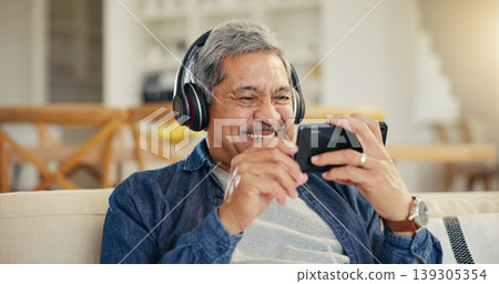 Senior, man and headphone with phone in living room for streaming, entertainment and mobile app. Elderly person, smile and retirement with technology with laugh for funny video, movie or film in home Senior, man and headphone with phone in living room for streaming, entertainment and mobile app. Elderly person, smile and retirement with technology with laugh for funny video, movie or film in home 139305354