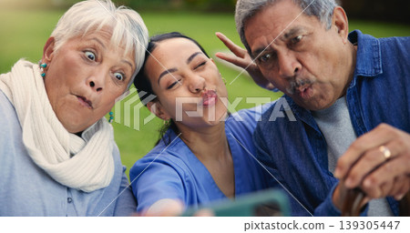 Selfie, peace sign or funny face with a nurse and old couple outdoor in an assisted living garden together. Comedy, support or wellness with a senior man, woman and young caregiver in the backyard Selfie, peace sign or funny face with a nurse and old couple outdoor in an assisted living garden together. Comedy, support or wellness with a senior man, woman and young caregiver in the backyard 139305447