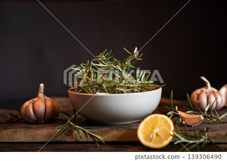 Fresh Rosemary Sprigs with Garlic and Lemon on Wooden Cutting Board 139306490