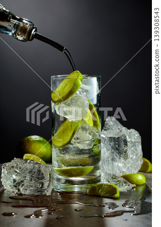 Gin is poured from a bottle into a glass with ice and lime slices. Gin is poured from a bottle into a glass with ice and lime slices. 139308543