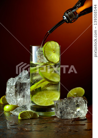 Vodka is poured from a bottle into a glass with ice and lime slices. Vodka is poured from a bottle into a glass with ice and lime slices. 139308544