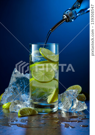 Gin is poured from a bottle into a glass with lime slices and crushed ice. Gin is poured from a bottle into a glass with lime slices and crushed ice. 139308547