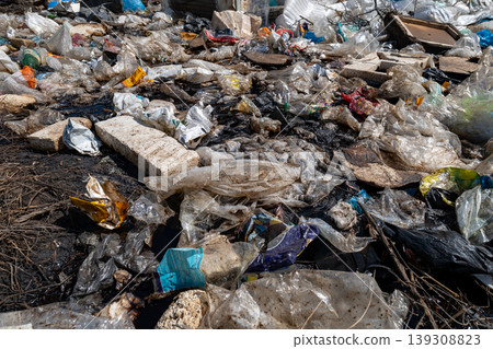Various pieces of plastic and garbage are scattered across a landfill site in an urban location during daylight hours 139308823