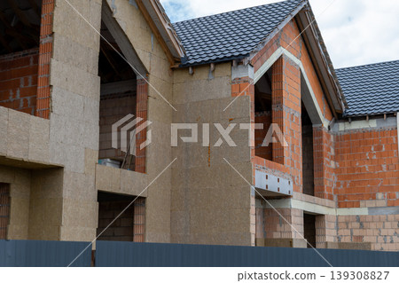 Workers are building new houses at a construction site. The walls are partially finished with visible bricks and materials 139308827