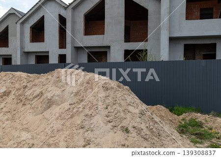 Construction workers prepare sand on the site while close to new buildings. The area shows dirt and building materials with a fence 139308837