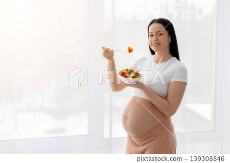 Pregnant young woman eating fresh vegetable salad, representing healthy eating habits Pregnant young woman eating fresh vegetable salad, representing healthy eating habits 139308846