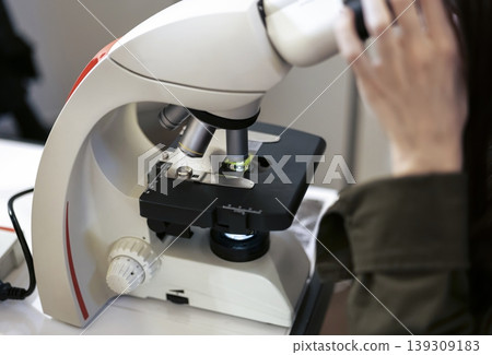 Person observing a sample under a binocular microscope, emphasizing microscopy techniques and detailed scientific examination 139309183