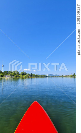 Red paddleboard in the middle of a calm river under a clear blue sky. Summer water sport, mental vitality, burst of energy. Red paddleboard in the middle of a calm river under a clear blue sky. Summer water sport, mental vitality, burst of energy. 139309187