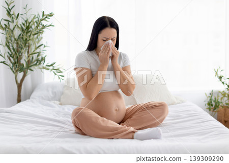 Pregnant woman sneezing into tissue, illustrating cold symptoms, immunity challenges during pregnancy Pregnant woman sneezing into tissue, illustrating cold symptoms, immunity challenges during pregnancy 139309290