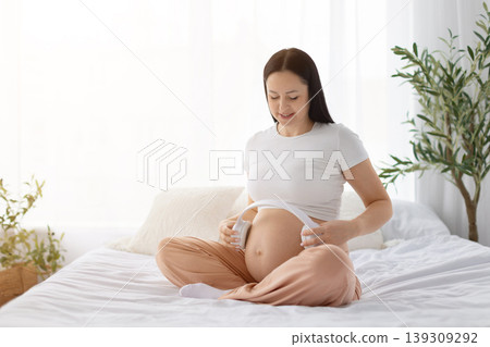 Pregnant woman placing headphones on belly, representing prenatal bonding through music 139309292